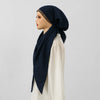 Una modelo vistiendo un hiyab azul marino con una cinta para la cabeza de borde dorado y una blusa de color crema.