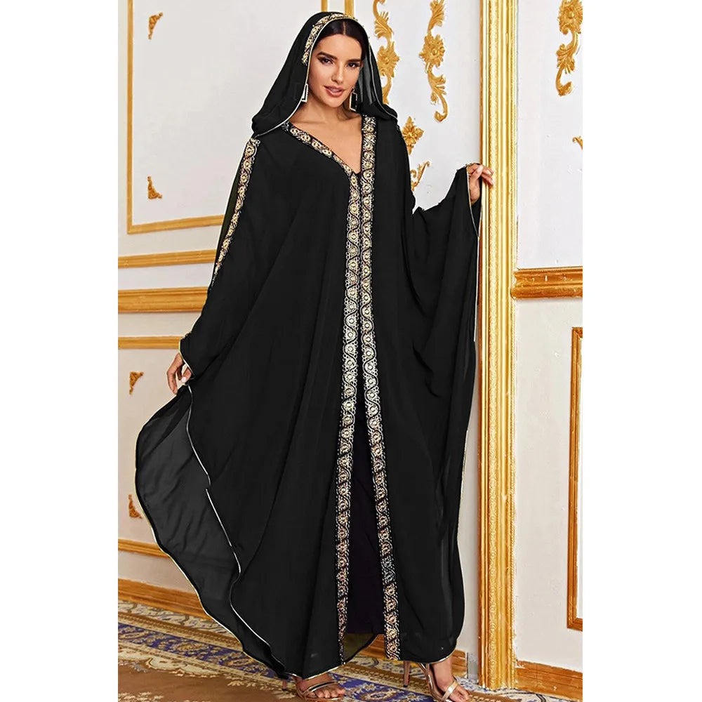 Una modelo vistiendo un abaya maxi negro y fluido con mangas de murciélago y bordado dorado contra un fondo claro.