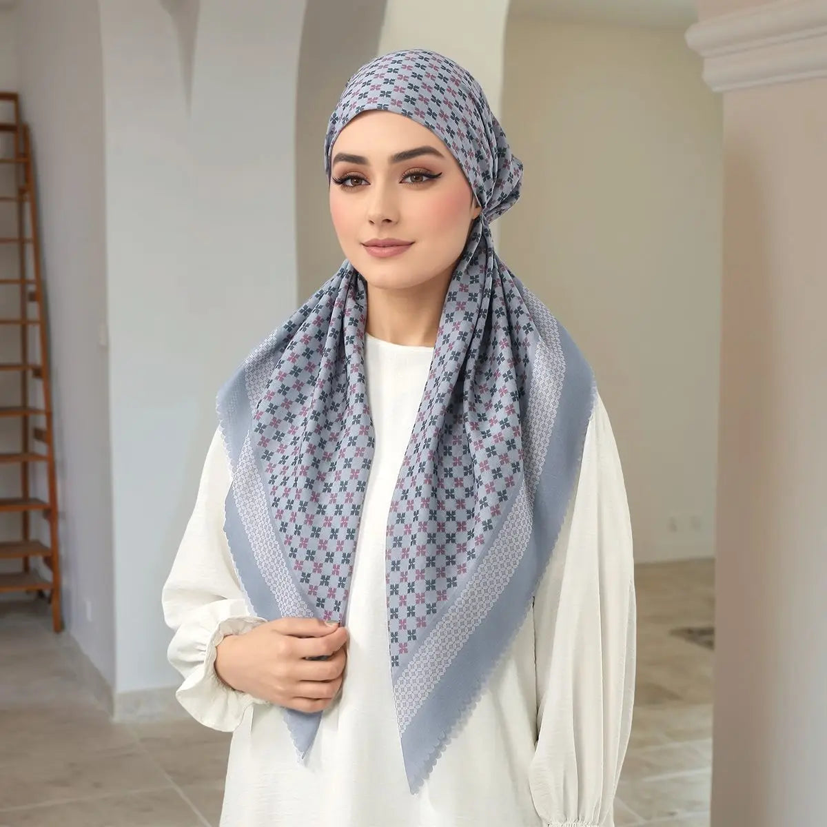 Eine Frau trägt einen hellblauen floralen Voile-Hijab und ein weißes Oberteil.