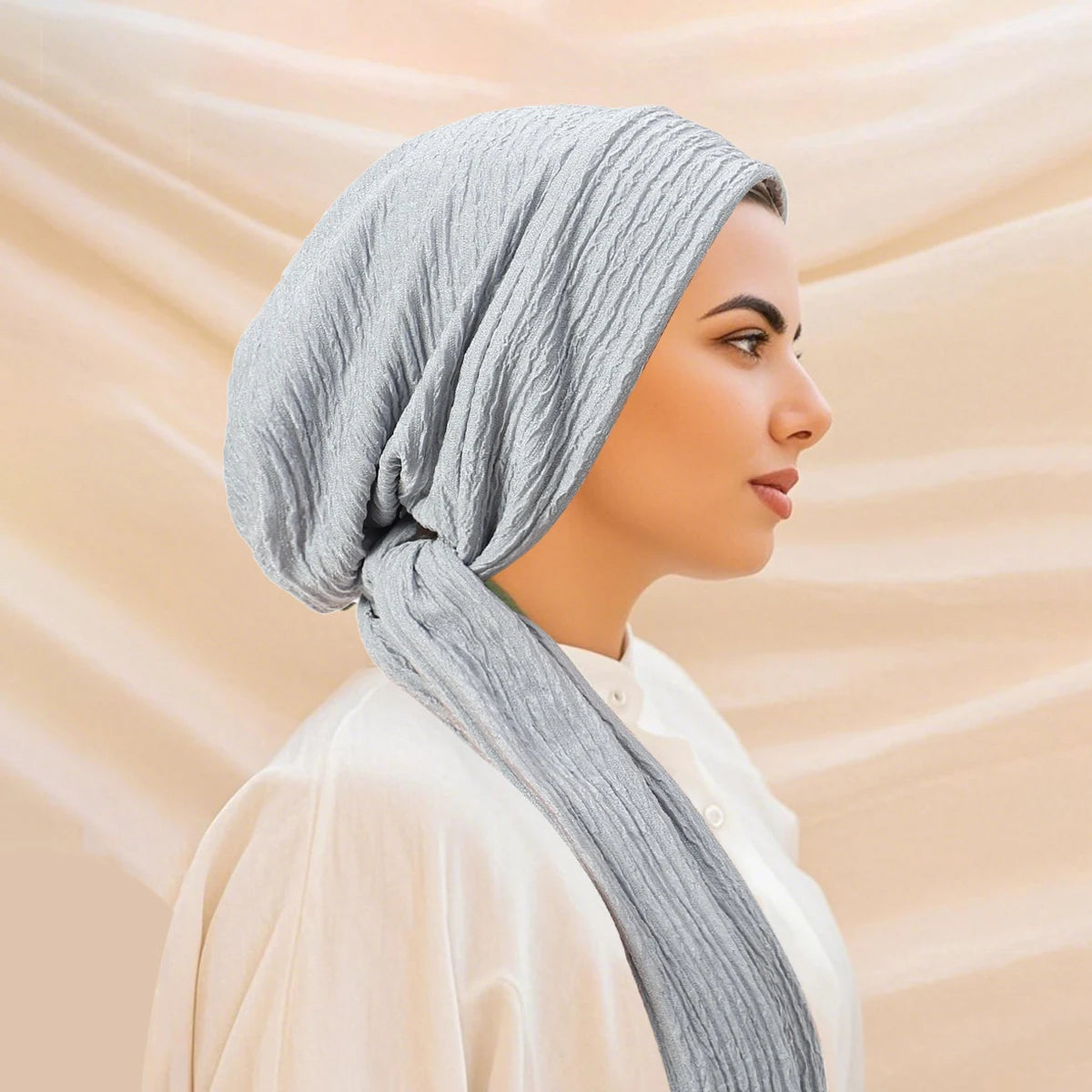 A woman wearing a solid gray turban hijab cap and a cream-colored top, shown in profile.