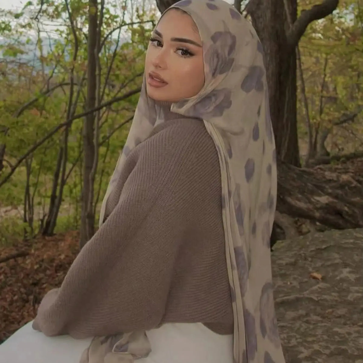 Une femme portant un foulard de coton imprimé floral dans des tons beige et violet à l'extérieur.
