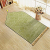 Un tapis de prière vert clair embossé avec une pompon doré posé sur un sol en bois.