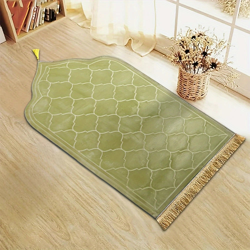 Un tapis de prière vert clair embossé avec une pompon doré posé sur un sol en bois.