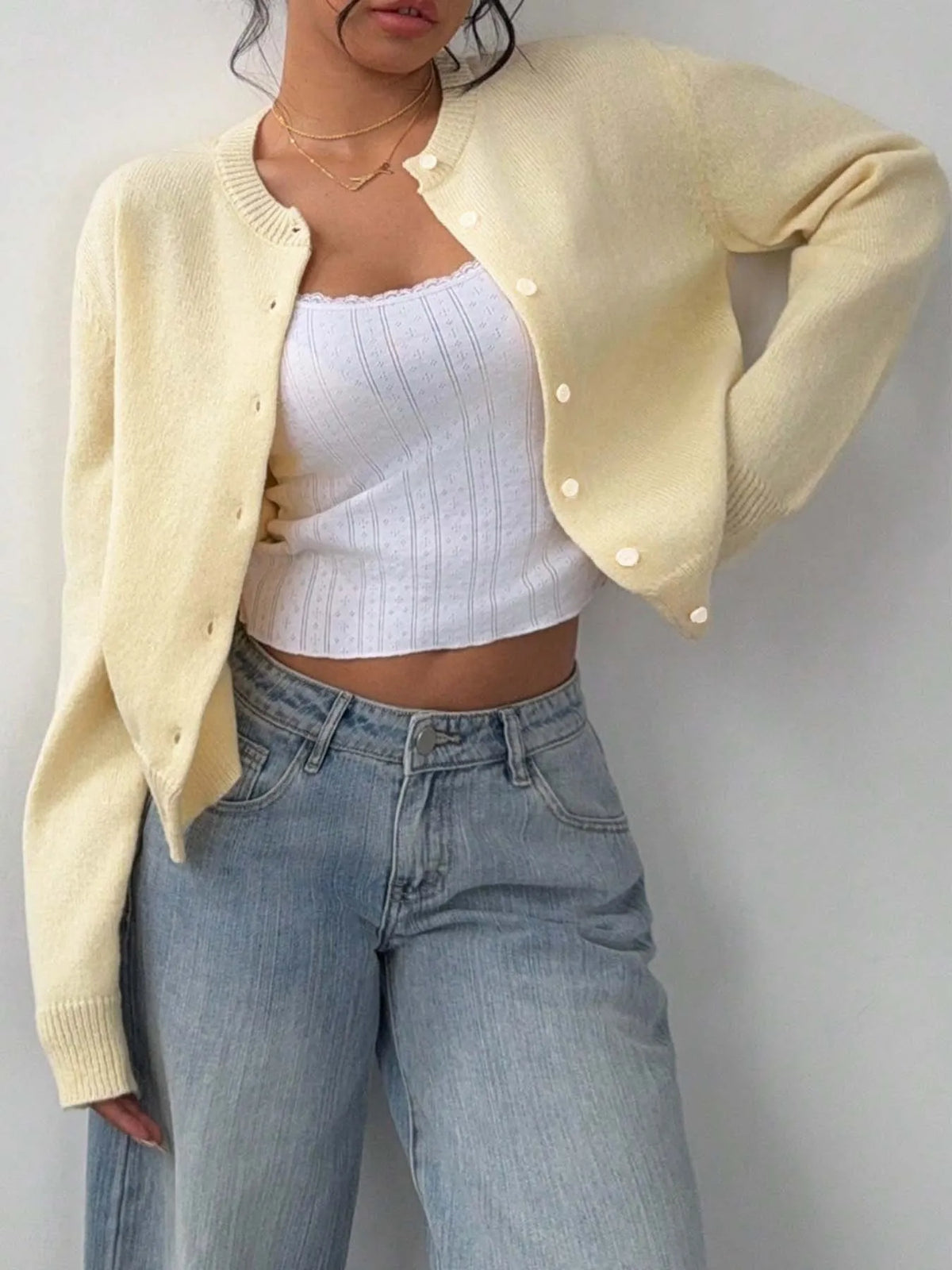 Une femme portant un pull en tricot jaune sur un haut côtelé blanc et un jean bleu.