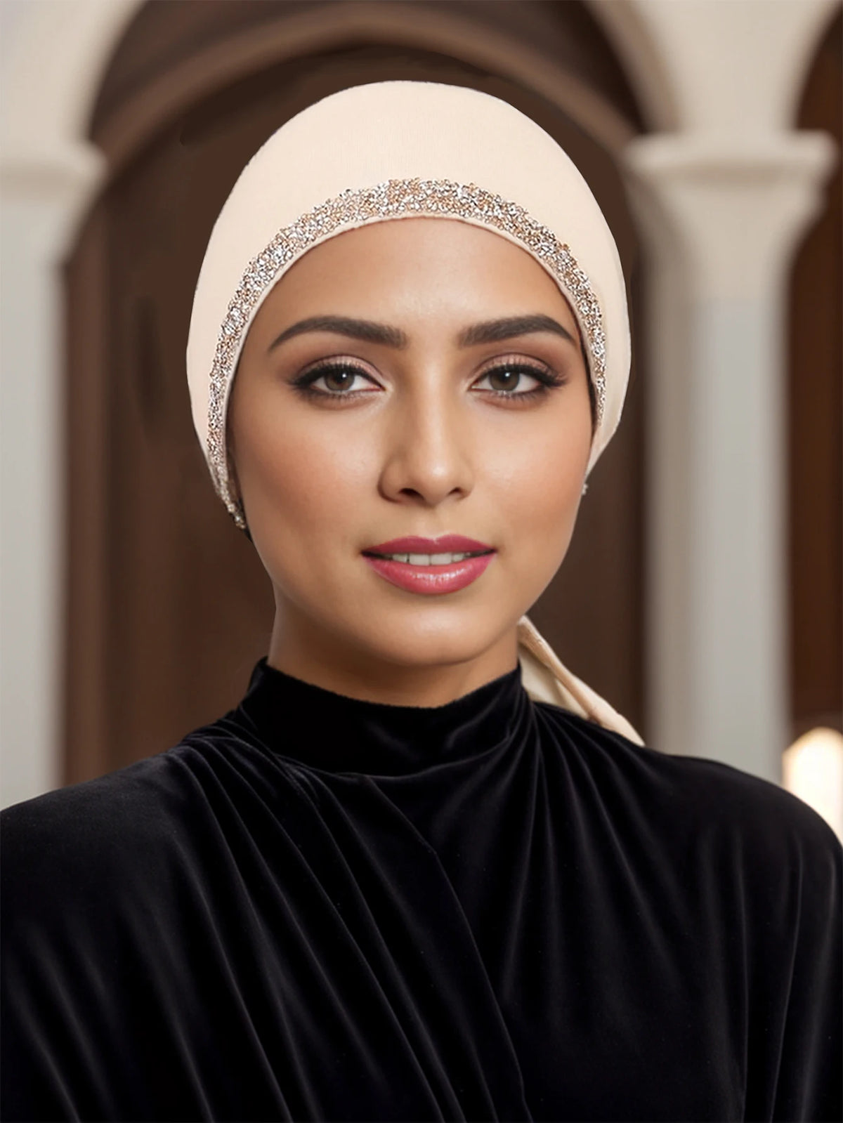 Eine Frau trägt einen beige Hijab mit funkelnden Strass und einem schwarzen Samt-Oberteil.