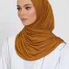 Eine Frau trägt einen einfarbigen braunen Jersey-Hijab und ein weißes Oberteil.