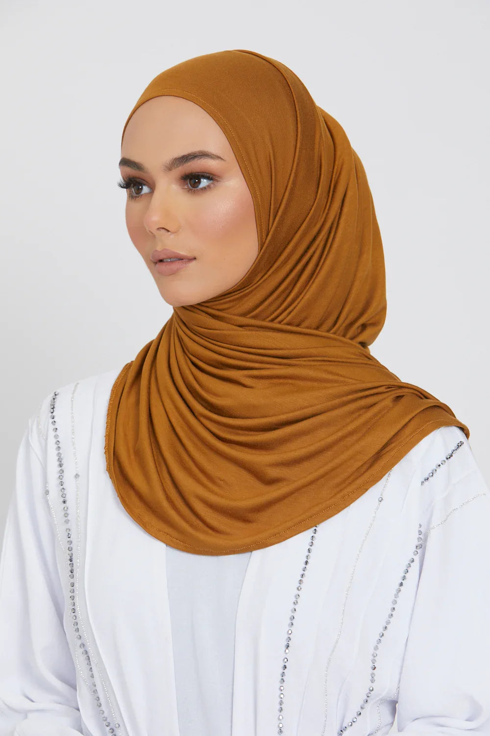 Eine Frau trägt einen einfarbigen braunen Jersey-Hijab und ein weißes Oberteil.