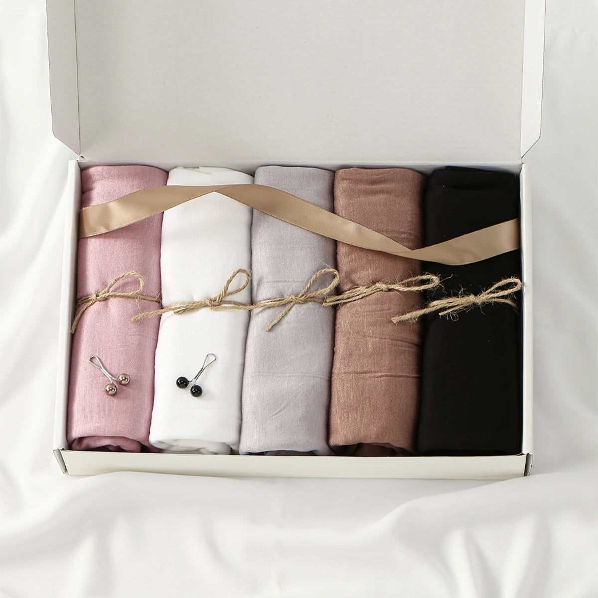 Eine Box mit fünf Jersey-Hijab-Schals in Pink, Weiß, Beige und Schwarz, mit natürlichen Binden