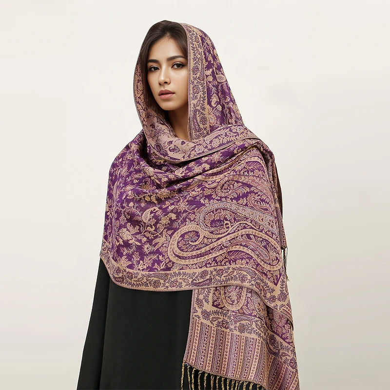 Una mujer modela un pañuelo pashmina de lujo con estampado morado y dorado sobre su cabeza y hombros.
