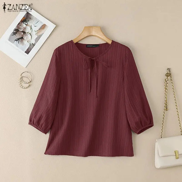 A maroon, vertically striped blouse with a tie-front detail is displayed on a wooden hanger against a light background.
