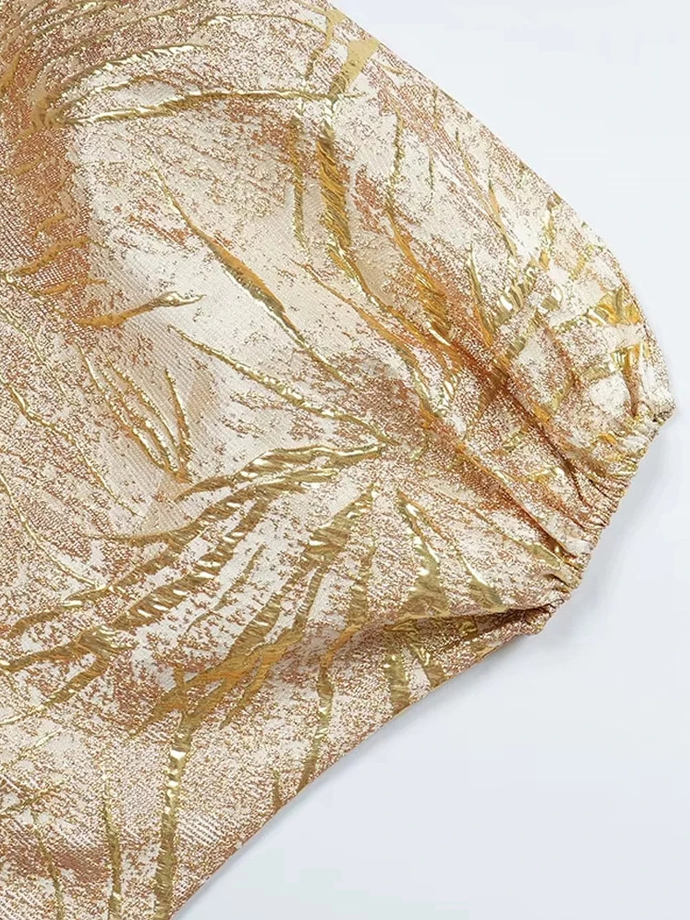 Primer plano de tela con lentejuelas doradas y patrón texturizado, posiblemente parte de un vestido largo o pañuelo.