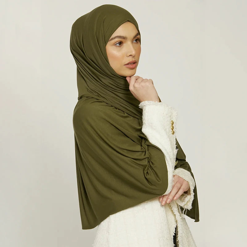 A woman wearing an olive green stretchy jersey plain hijab scarf with a white textured sleeve.