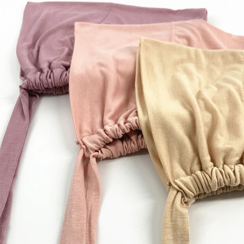 Drei innere Hijab-Bonnet-Bänder in Mauve, staubrosa und Beige auf weißem Hintergrund gestapelt.