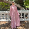 A woman wearing a long pink modest dress and matching headscarf outdoors.