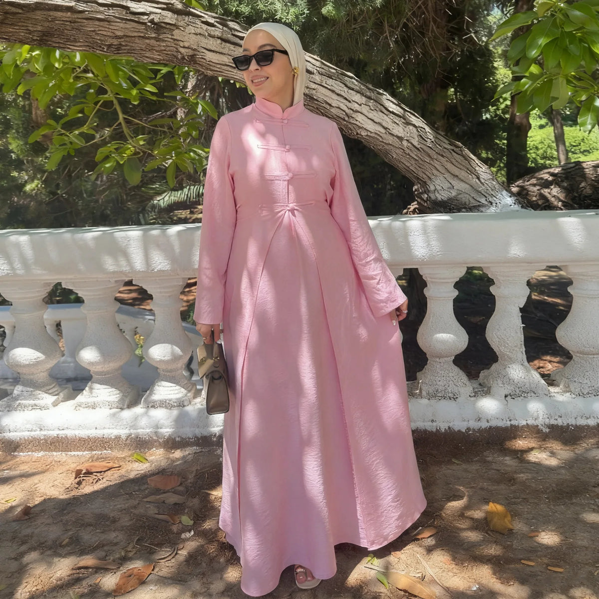 A woman wearing a long pink modest dress and matching headscarf outdoors.