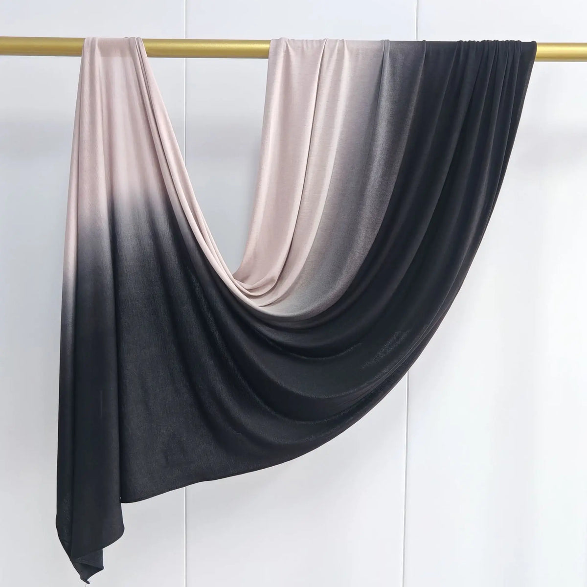 Pañuelo de algodón en degradado gris oscuro y rosa empolvado colgado en una varilla de madera.