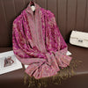 Pañuelo pashmina de lujo morado y rosa vibrante drapeado sobre una superficie de cuero marrón.