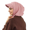 Une femme portant un bonnet hijab couleur rose poudré et un haut marron.