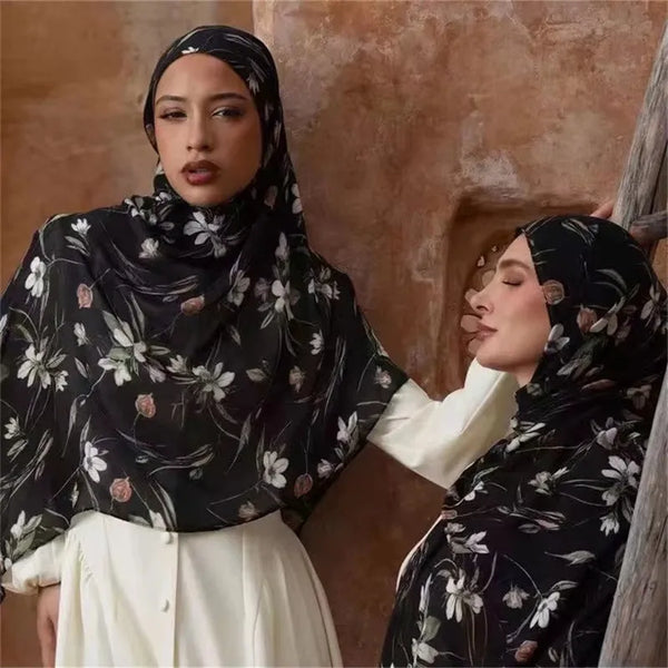 A woman wearing a black floral hijab scarf is shown in a portrait against a textured wall.