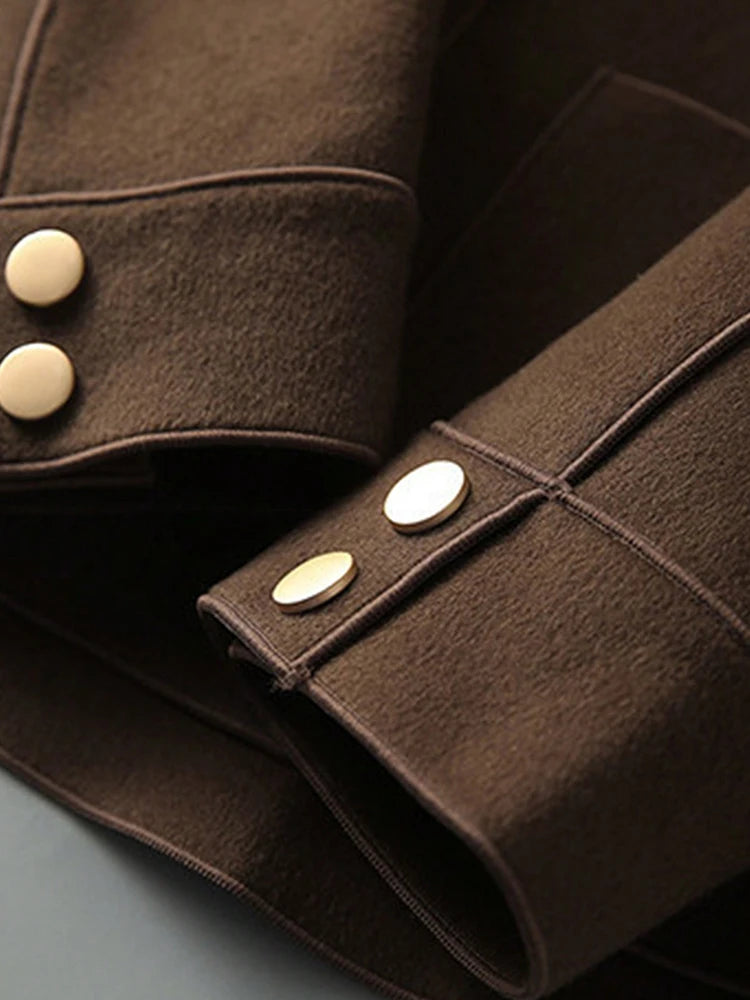 Gros plan sur la manche d'un manteau en laine brun foncé avec des boutons de laiton.