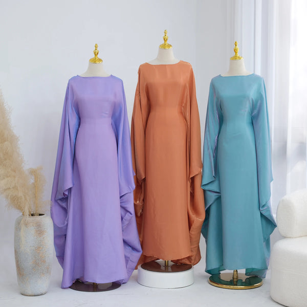 Three elegant kaftan dresses in purple, orange, and teal displayed on mannequins.