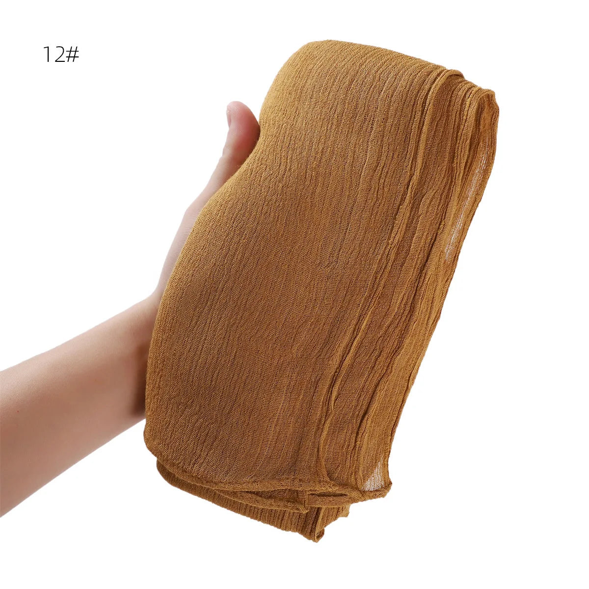 Une main tient un châle en crêpe rayon brun moutarde, plié et drapé.