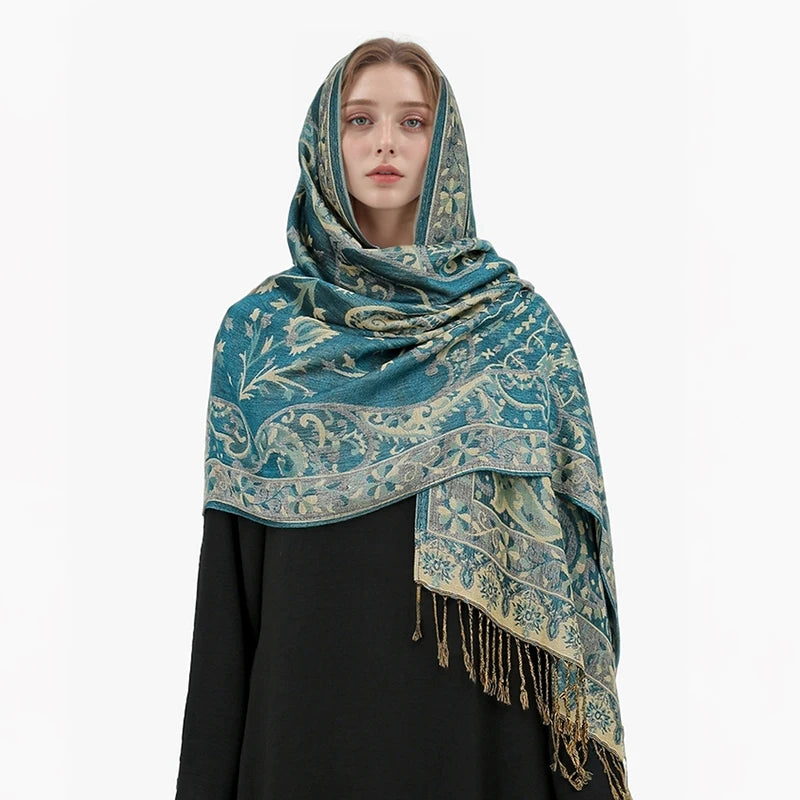 Una mujer vistiendo un pañuelo de pashmina de lujo con estampado verde azulado y dorado sobre una prenda negra.