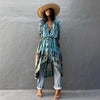Eine Frau in blau-schwarzem Tie-Dye Kimono-Überkleid und breiter Strohhut vor einer grauen Wand.
