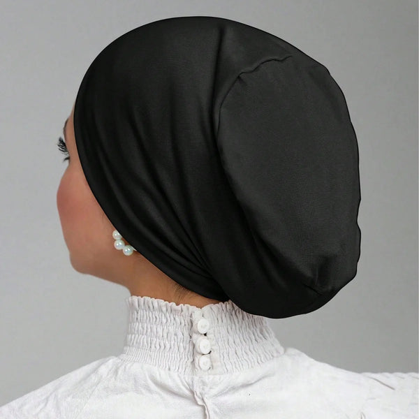A close-up profile of a woman wearing a black stretch jersey inner hijab cap with pearl accents.