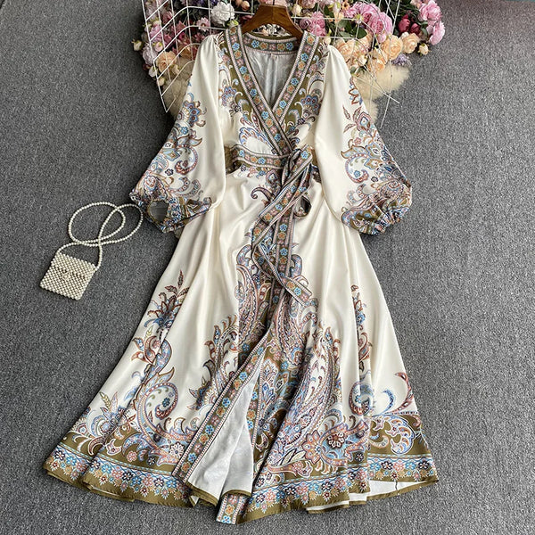 A white maxi dress with floral lace-up detailing and intricate brown and blue embroidery is displayed on a hanger.