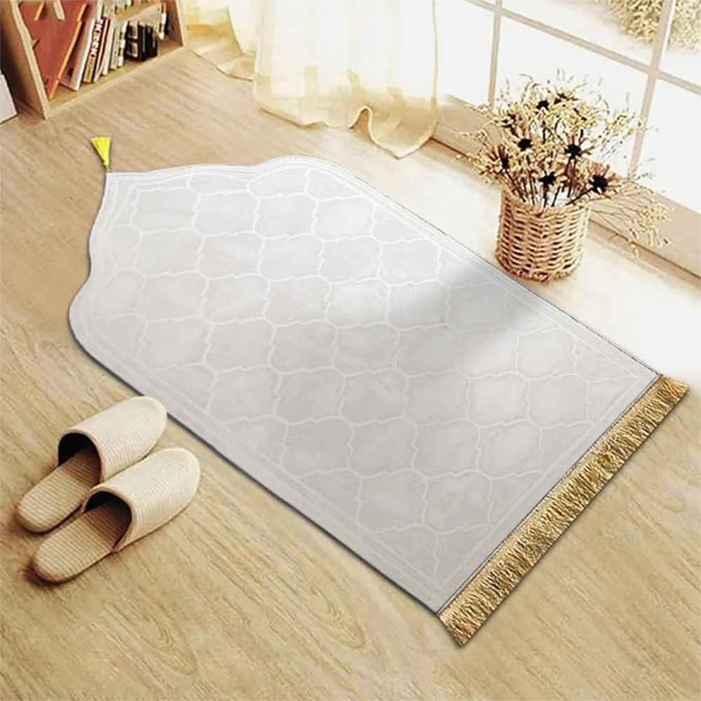 Rechteckige beige Gebetsmatte mit goldfarbener Fransenborte auf hellem Holzfußboden.