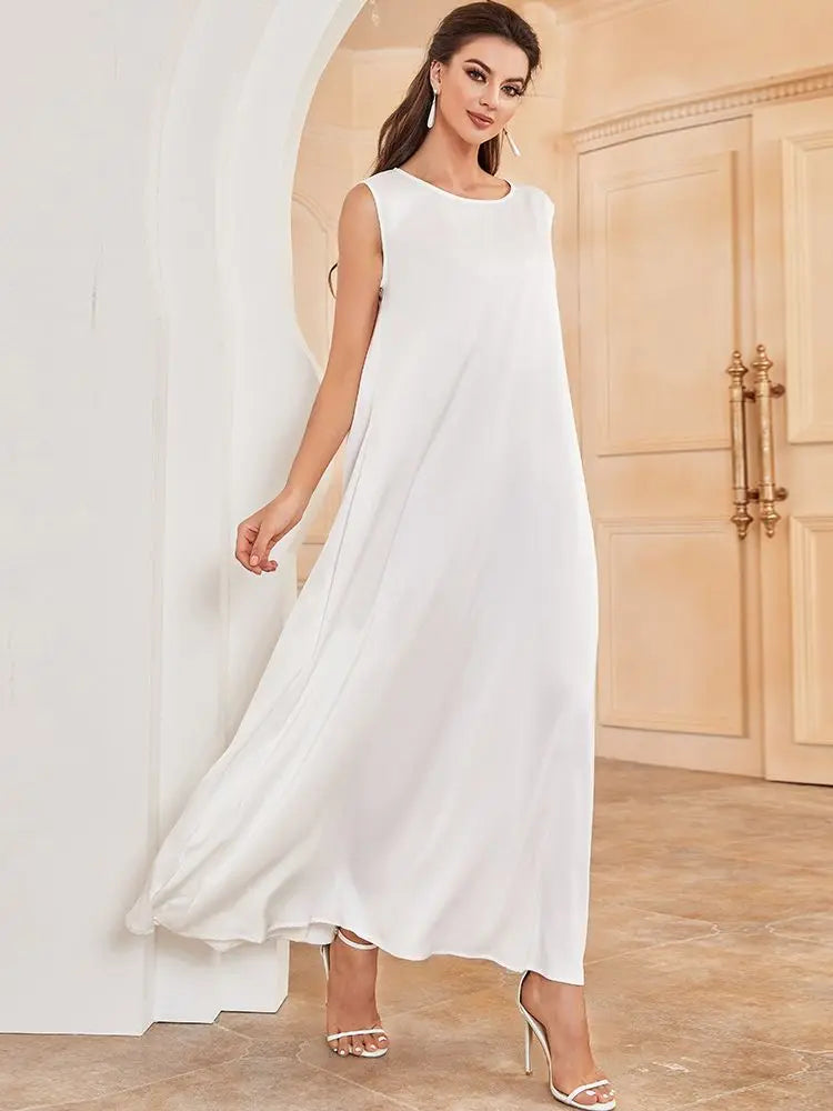 A woman wearing a white flowing modest abaya dress standing in a light-colored room.