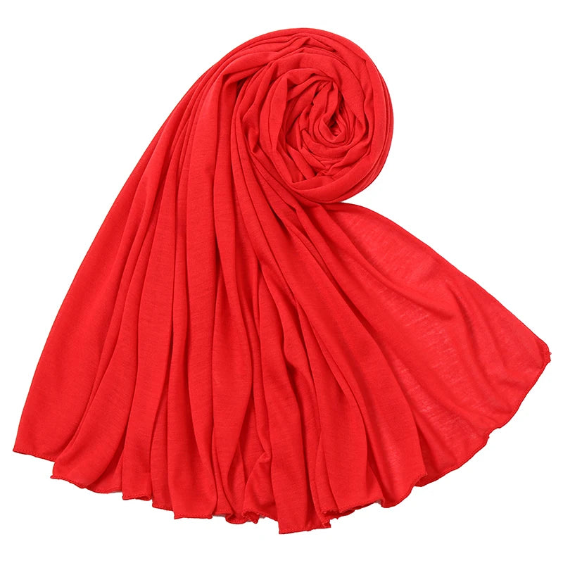 Ein leuchtend roschroter Baumwoll-Jersey-Hijabschal, gerollt und drapiert, zeigt seine weiche Textur.