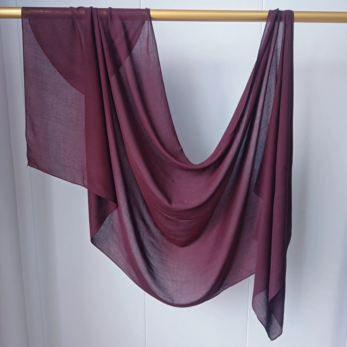 Foulard hijab uni couleur marron foncé drapé sur un cintre en bois.