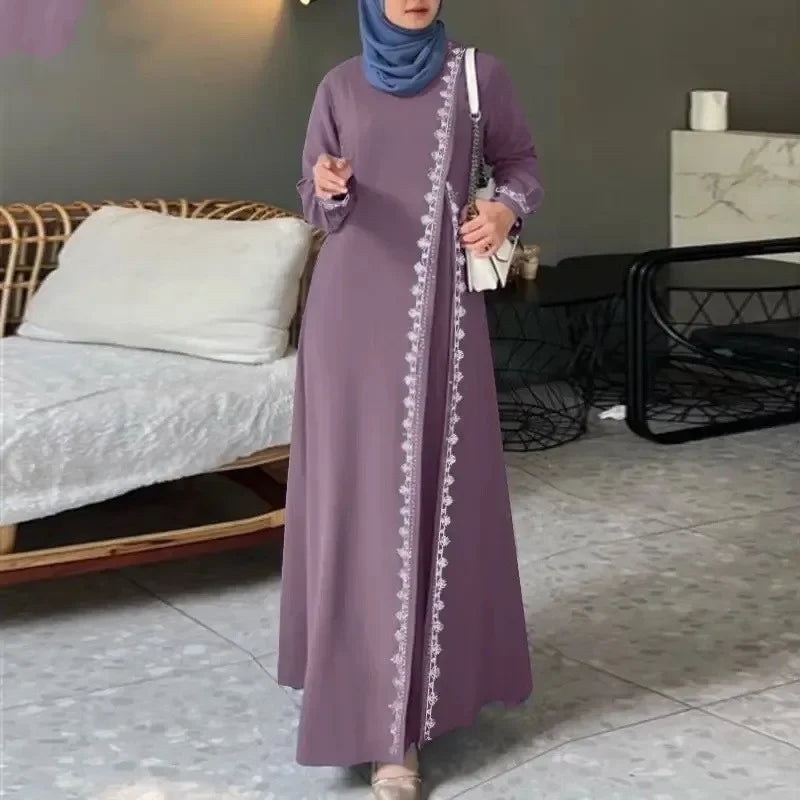 Eine Frau in einem langen, mauvefarbenen Spitzen-Abaya-Kleid mit Stickereien steht in einem modernen Innenraum.