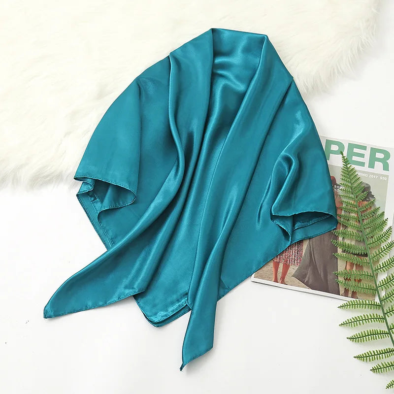 A teal silk satin hijab scarf draped over a white fluffy surface.