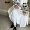 Une femme portant une abaya musulmane blanche brodée avec des bordures noires et des mocassins noirs.
