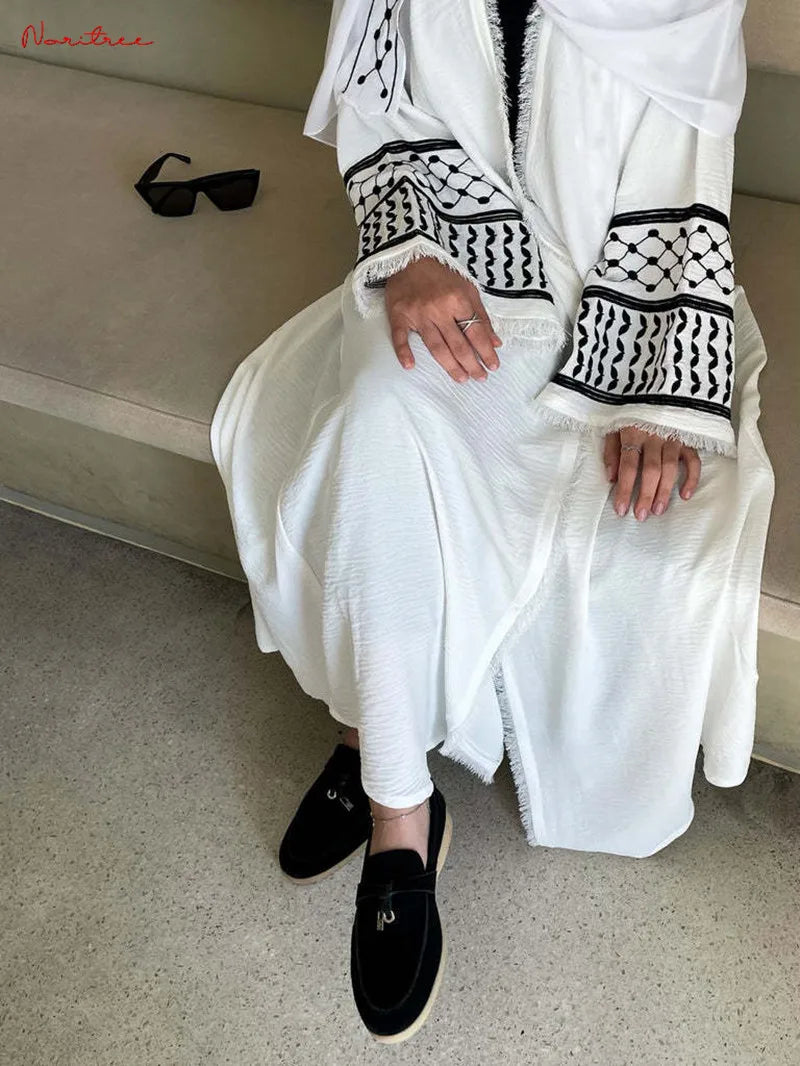 Une femme portant une abaya musulmane blanche brodée avec des bordures noires et des mocassins noirs.