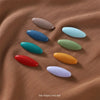 A set of eight solid color brooch pins in various shades including pink, blue, green, and red, displayed on a brown fabric.