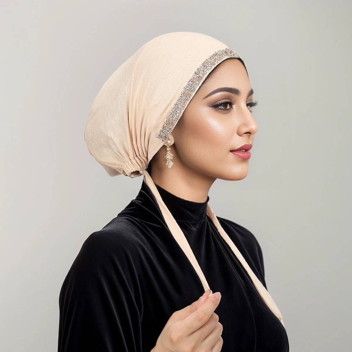 Eine Frau mit beigem Strass-Hijabschal und schwarzem Oberteil, im Profil gezeigt.