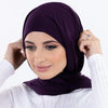 Une femme portant un hijab instant en mousseline violet foncé et un haut blanc, regardant l'appareil photo.