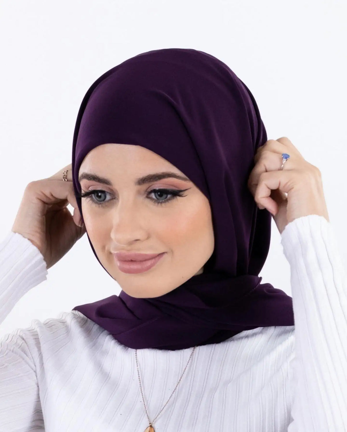 Une femme portant un hijab instant en mousseline violet foncé et un haut blanc, regardant l'appareil photo.