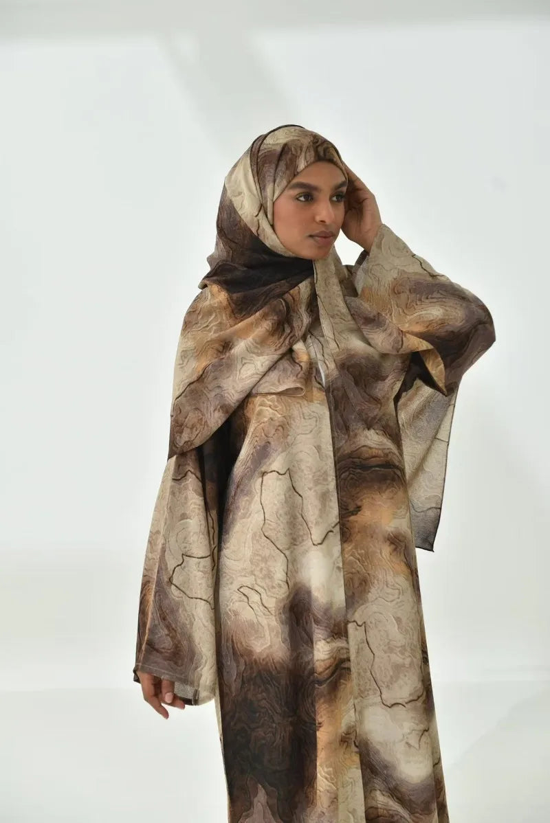 Eine Frau trägt ein elegantes Blumen-Abaya und Hijab-Set in erdigen braunen Tönen.