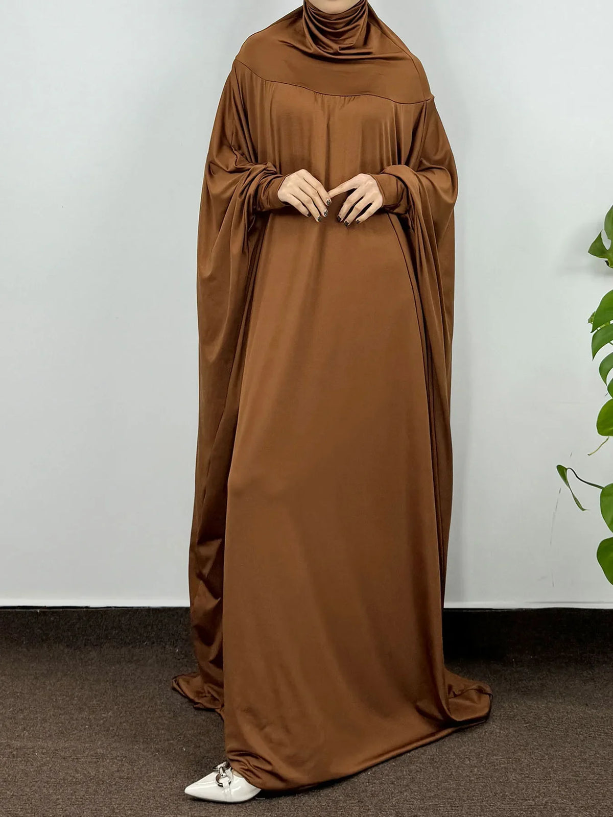 Una mujer vistiendo una abaya marrón lisa y fluida con capucha, mangas largas y cuello alto.