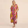 Eine Frau modelliert ein gelbes marokkanisches Batwing Kaftan-Überkleid mit rosa und lila Blumenmustern.