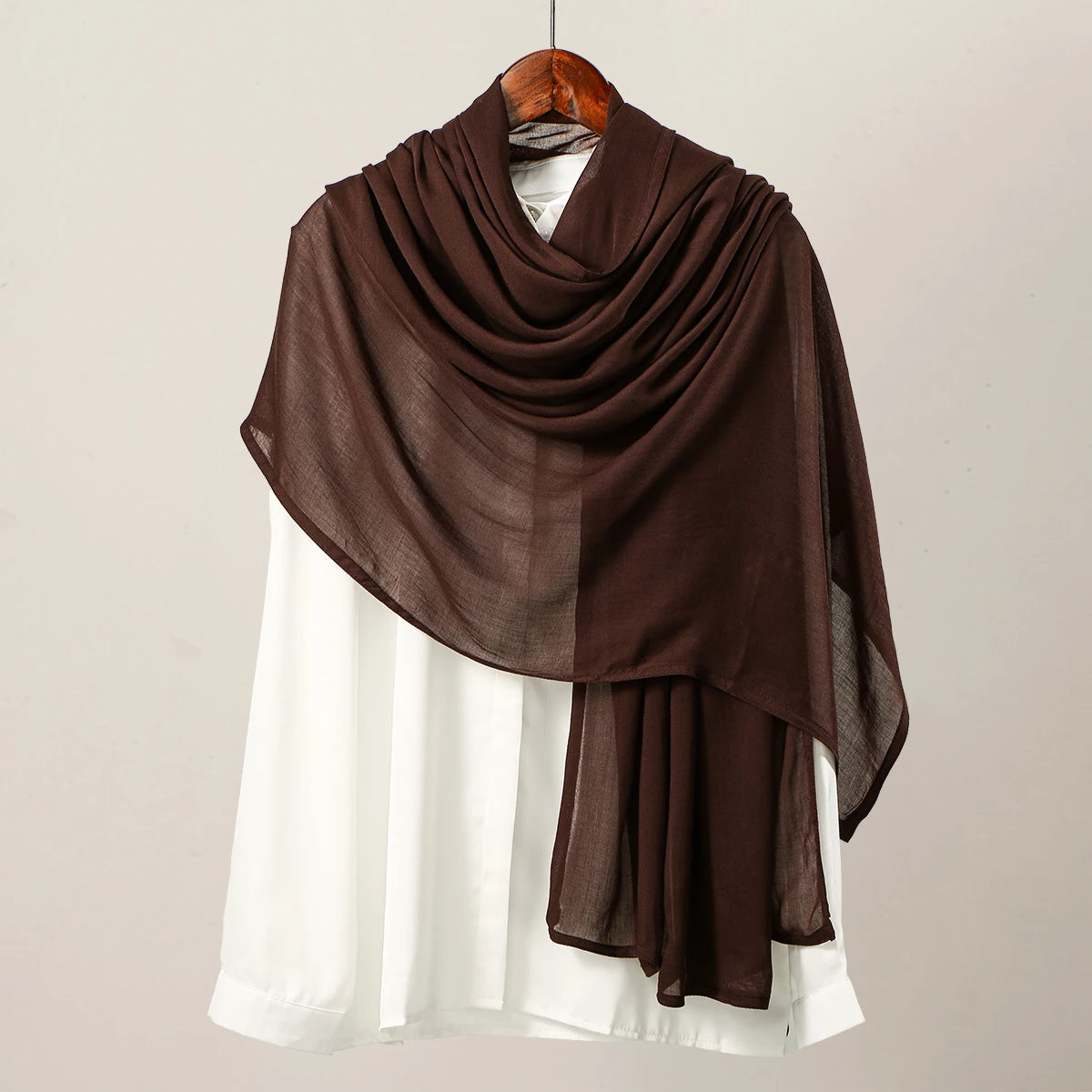 Pañuelo de hijab de modal color marrón oscuro drapeado sobre una prenda blanca.
