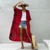 Eine Frau in einem rot-schwarz gemusterten Kimono-Überwurf über einem weißen Top und Jeansshorts, vor einem hellgrauen Hinter