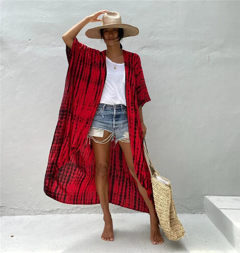 Eine Frau in einem rot-schwarz gemusterten Kimono-Überwurf über einem weißen Top und Jeansshorts, vor einem hellgrauen Hinter