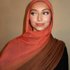 Eine Frau trägt einen orangefarbenen Hijab-Schal in Farbverlauf über Kopf und Schultern.