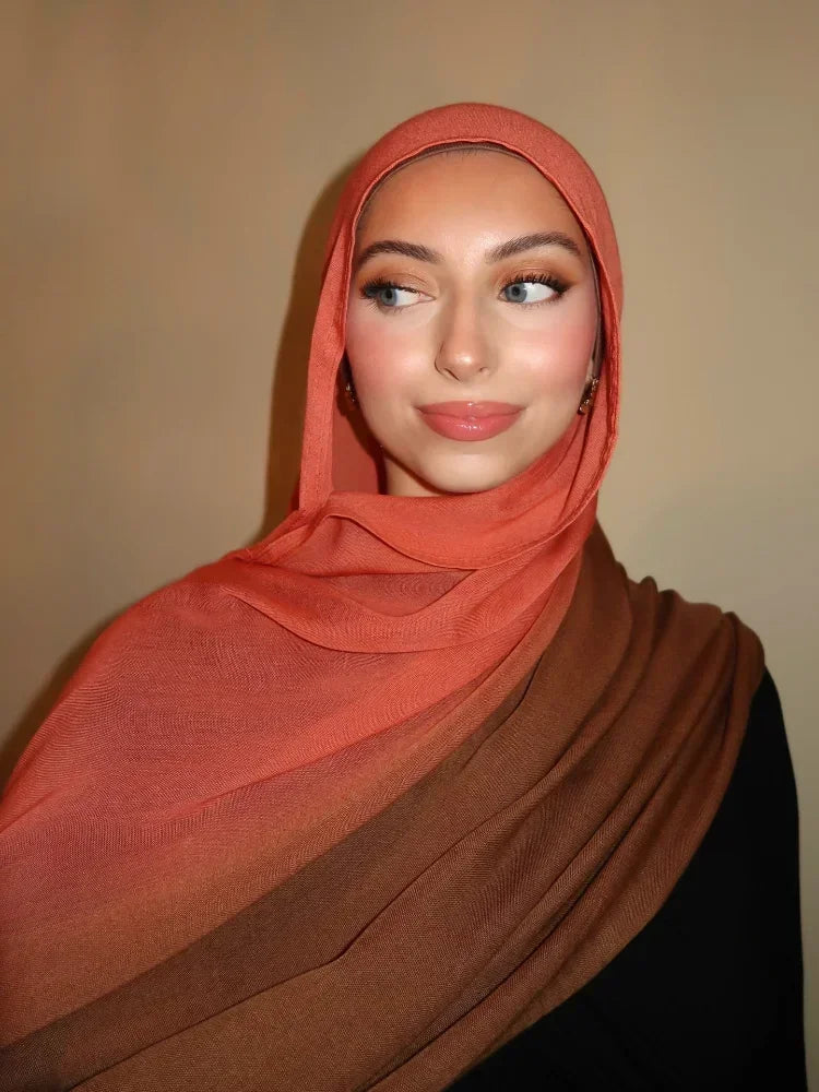 Eine Frau trägt einen orangefarbenen Hijab-Schal in Farbverlauf über Kopf und Schultern.